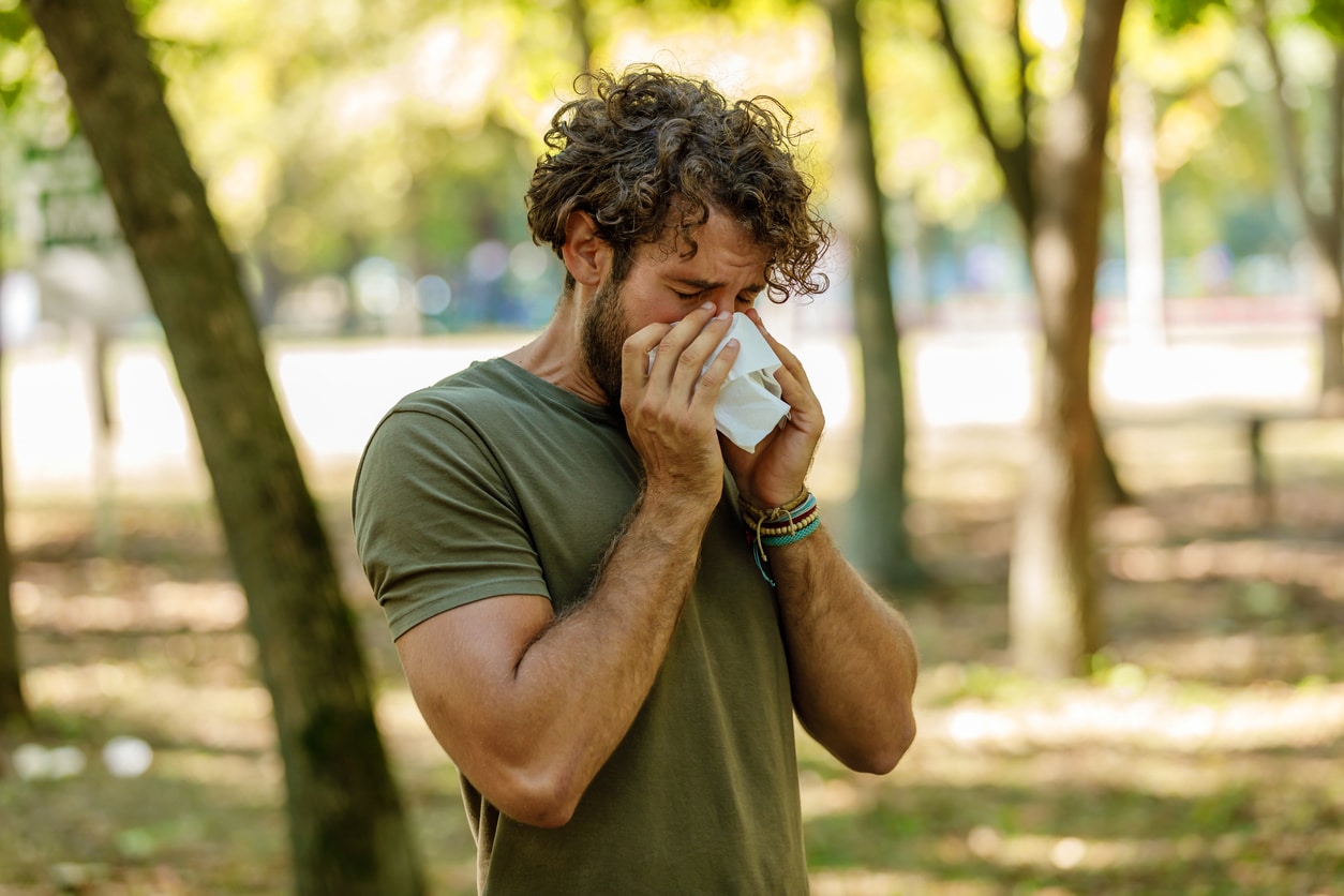 Man sneezing into a tissue at the park
